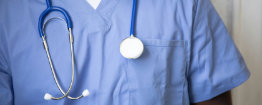 A person wearing light blue medical scrubs with a stethoscope around their neck, shown from the shoulders down.