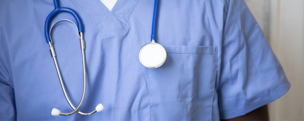 A person wearing light blue medical scrubs with a stethoscope around their neck, shown from the shoulders down.