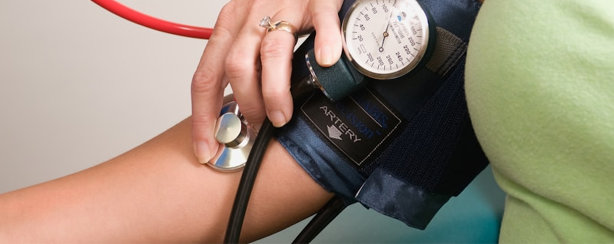 A healthcare professional measures a persons blood pressure using a sphygmomanometer and stethoscope on the persons arm.