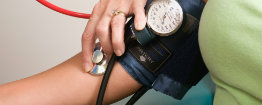 A healthcare professional measures a persons blood pressure using a sphygmomanometer and stethoscope on the persons arm.