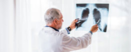 A doctor holds up and examines a chest X-ray in a brightly lit room.